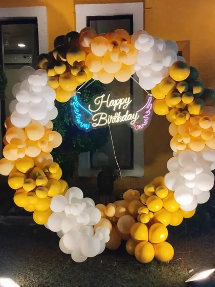 A beautiful yellow and white balloon ring with a neon sign, perfect for an outdoor evening birthday celebration.