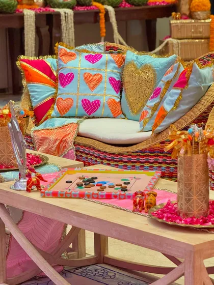 A detailed shot of the custom-designed cushions and playful elements from a Garba event. A hand-painted carrom board sits on the table, reflecting the nostalgic and fun theme of the celebration.