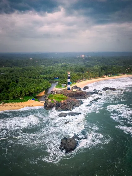 An aerial view of the Kaup lighthouse standing strong against the powerful waves of the monsoon season. This perspective shows the dramatic meeting of land and sea on the Karnataka coast.