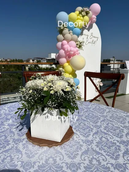 A table centerpiece with fresh white flowers, with the pastel balloon backdrop of the bunny-themed shower in the background.