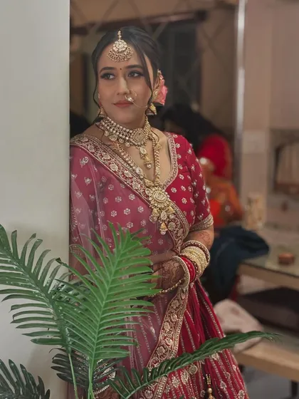 A candid shot of the bride in her stunning red lehenga. The makeup is soft and elegant, with a focus on creating a natural, radiant glow that looks beautiful in any light.