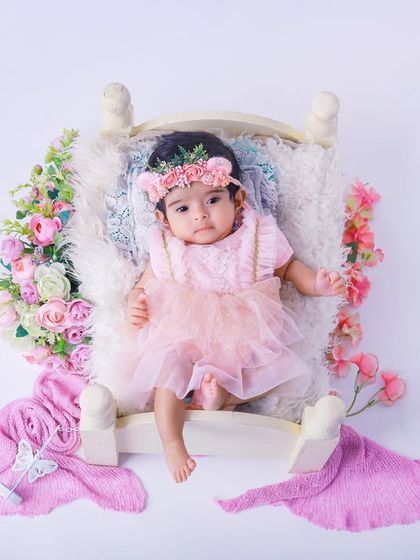 An overhead view of a baby girl in a lovely pink dress, resting on a tiny bed surrounded by flowers. We carefully arrange each detail to create a perfectly composed shot.