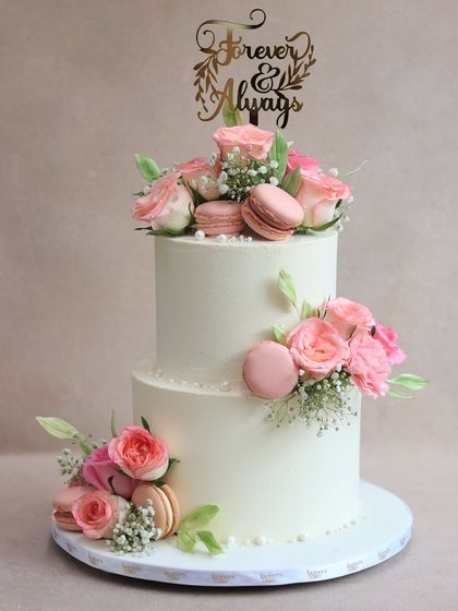 A repeat of a beloved design, this two-tiered white cake with fresh pink roses and macarons is a popular choice for celebrating love. Its classic elegance makes it perfect for weddings and anniversaries.