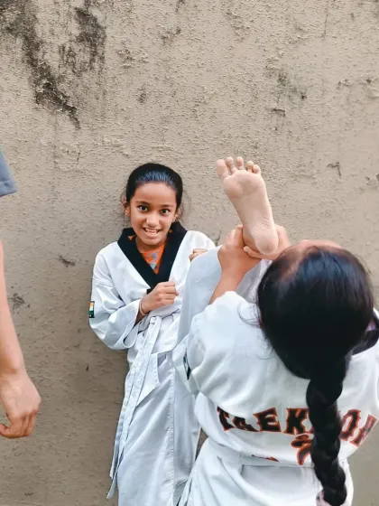 Two students help each other with high-kick stretches. The smiles on their faces show that hard work can also be fun, especially when you're training with friends.