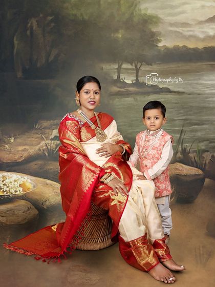 A precious family portrait with the older sibling. The mother-to-be is seated in a traditional red and white saree, with her son standing beside her.