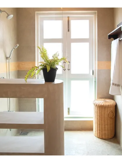 This sun-lit bathroom in a Goa villa uses Vanilla stone tiles and Jaisalmer stone to create a warm, natural feel. A monolithic cream IPS divider separates the shower and WC areas, maintaining an open and airy atmosphere.