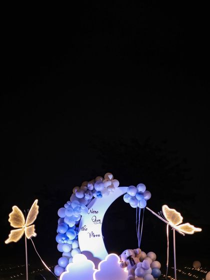 For outdoor decor, I created this beautiful photo spot featuring a crescent moon prop with the phrase "We love you to the moon". It's surrounded by blue balloons and illuminated butterfly props.