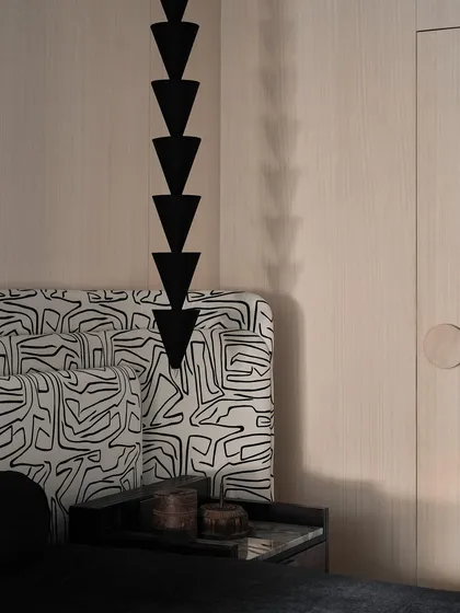 A detail shot of the master bedroom, focusing on the stacked, geometric pendant light and the intricate pattern of the headboard fabric.