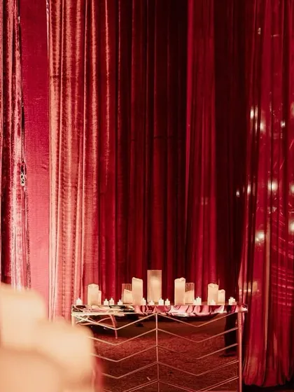 An entryway detail from 'The Scarlet Soirée', with mirrored consoles, dozens of candles, and dramatic red velvet draping creating a glamorous and moody welcome.