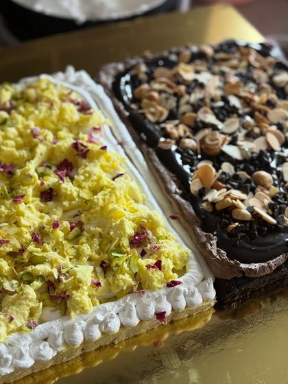 A close-up of a delicious half and half sheet cake. One side is a traditional Indian-inspired Ras Malai cake, and the other is a decadent chocolate almond cake.