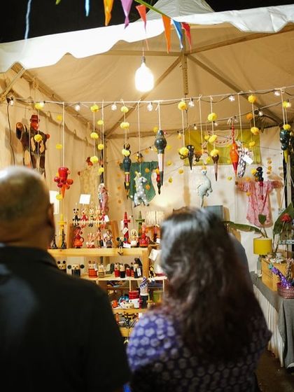 Visitors exploring a stall filled with colourful, handcrafted wooden toys and decor. The warm lighting and intricate items create a magical shopping experience.