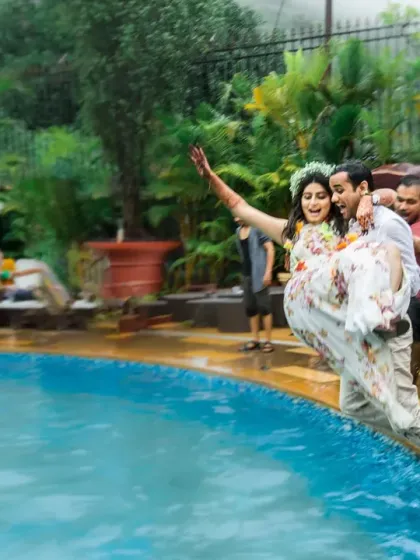 The groom carries his bride as they are about to be pushed into the pool by friends, a moment of fun and playful chaos.