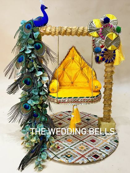 A divine Krishanji Jhula for Janmashtami. This design features a bright yellow quilted seat and a stunning arrangement of real peacock feathers, creating a majestic and traditional swing for Laddu Gopal.