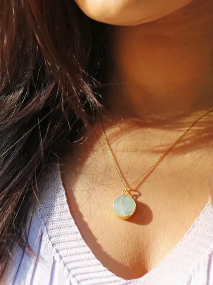 Golden hour light catches this delicate circular stone necklace beautifully. This image highlights the thin gold chain and the subtle texture of the gemstone, ideal for showcasing minimalist jewelry designs.