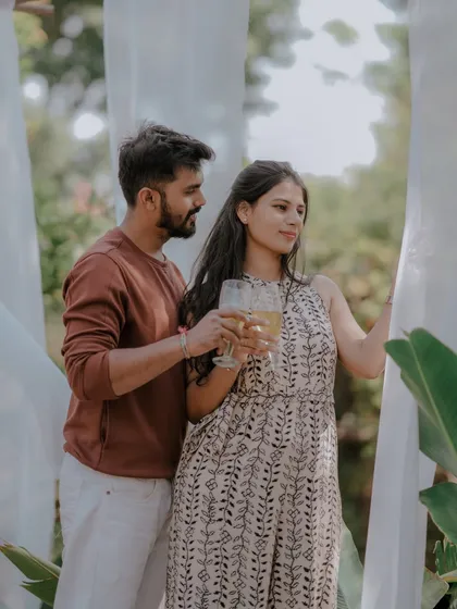 A celebratory toast to their future together. This shot captures a simple, happy moment during a relaxed outdoor pre-wedding session, framed by soft white drapes.