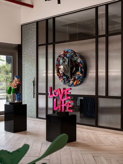 This installation view features a 'Love Life' sculpture, a reflective butterfly piece, and a Popeye figure. Together, they create a corner that is unapologetically pop, celebrating life with bold colors and iconic characters.