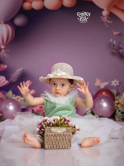A stylish little lady in a hat, ready to celebrate her first birthday in a beautiful purple floral setting.