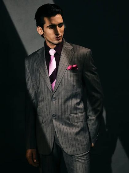 An interesting contrast on a blended woollen dark grey suit with deep purple pinstripes, paired with a pink tie for a pop of color.