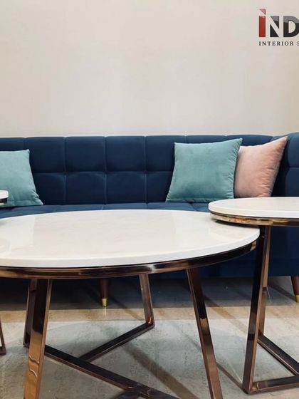 A close-up of the tufted navy blue sofa and the nested coffee tables. The tables feature a white marble top and rose gold legs, adding a touch of modern luxury.