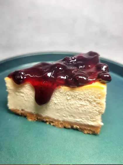 A perfect slice of our NYC-Style Cheesecake, topped with a generous amount of our homemade blueberry compote. The rich, dense cheesecake is balanced by the tartness of the berries.