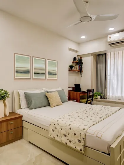 A tranquil bedroom from the same residence, featuring a light color palette and natural wood tones. The floral bedspread and serene wall art create a soft and peaceful atmosphere.