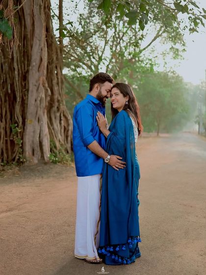 A full-length portrait showing the beautiful coordination of their traditional outfits against the backdrop of a massive banyan tree.