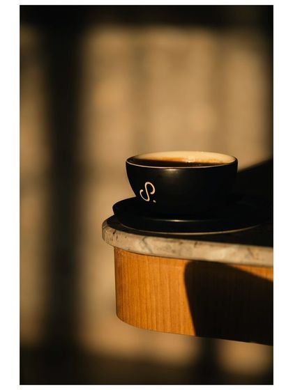 A cup of coffee sits on a marble table, bathed in the warm light of the setting sun. The beautiful shadows and golden tones create a peaceful and aesthetically pleasing image.
