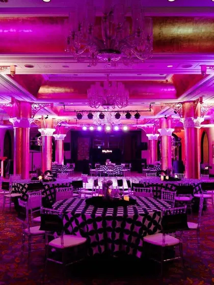 The ballroom at the Taj Mahal Palace transformed for Vijayshree and Omkar's Sangeet. The space was washed in vibrant pink and purple light, with custom-printed tablecloths and elegant chandeliers creating a glamorous party vibe.