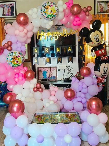 A cute Mickey and Minnie Mouse themed birthday setup with a pink, purple, and white balloon arch.