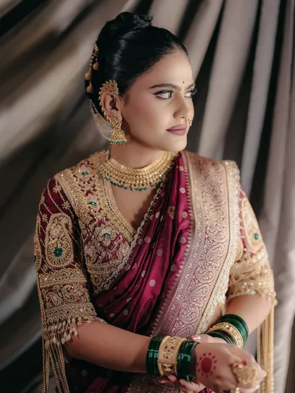 The regal posture of a Maharashtrian bride. Her makeup is flawless, with a focus on defined eyes and a matte lip that complements the rich maroon and gold of her attire.