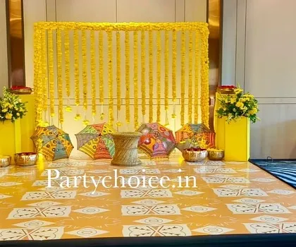 We designed this indoor Haldi setup with a dominant yellow theme. The backdrop is a curtain of marigold strings, complemented by colorful Rajasthani umbrellas and a custom-printed floor mat for a cohesive and cheerful look.