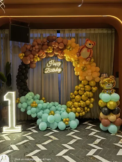 A stylish teddy bear themed first birthday with a unique color palette. The circular balloon arch in brown, gold, and mint green is paired with a light-up number '1' and bear-themed details.