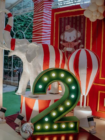 A close-up of the lit-up number '2' for the birthday boy, surrounded by a custom-painted elephant and a hot air balloon prop. I use marquee lights to add a touch of sparkle and highlight the milestone being celebrated.