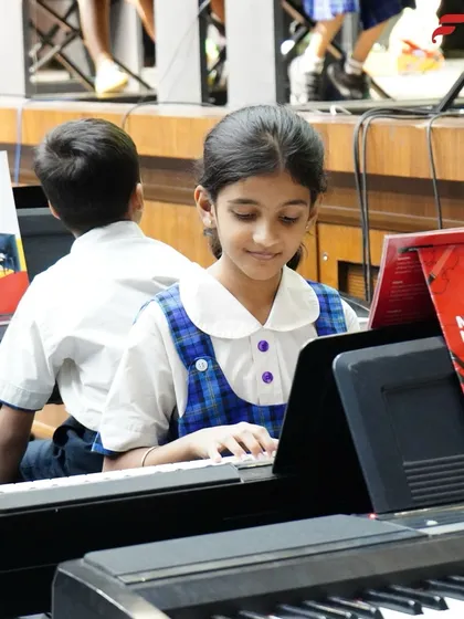 A close-up of a young student focused on her keyboard during a school recital. With our "My Music Handbook" and dedicated practice, students follow a structured curriculum that builds their skills progressively.