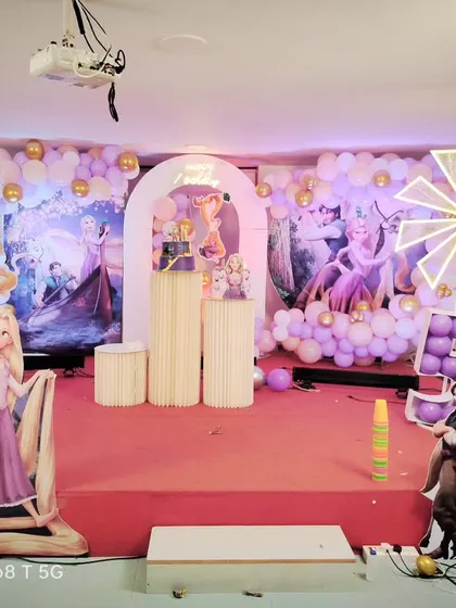 A full view of a Tangled themed birthday stage, complete with character cutouts of Rapunzel and Flynn Rider, themed backdrops, and a decorative white picket fence.