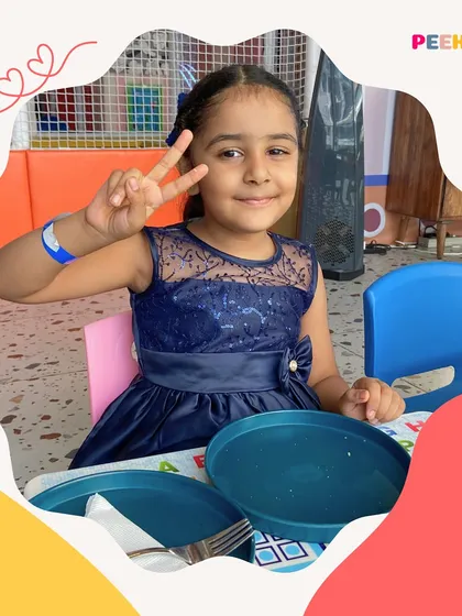 A happy young customer gives a peace sign while sitting at her table, ready to eat. Our kid-friendly plates and tables make mealtime fun and comfortable for our smallest guests.