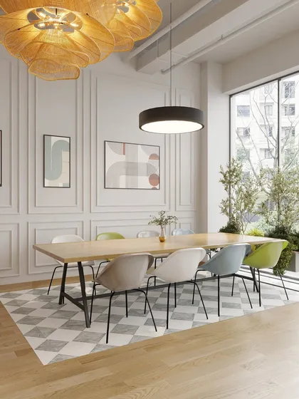 A collaborative table sits adjacent to the main reception, bathed in natural light from large windows. The classic wall molding and checkerboard rug add a touch of timeless elegance to the modern space.