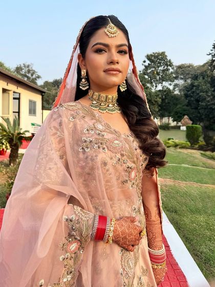 This bride is shining brighter than the sun on her wedding day. I created a radiant, minimal makeup look with open, wavy hair to match her pastel lehenga for a modern bridal style.
