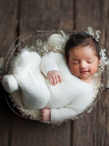 That little smile just melts my heart. Dressed in a soft white knit romper and nestled in a wire basket, this portrait captures a moment of pure, dreamy bliss.