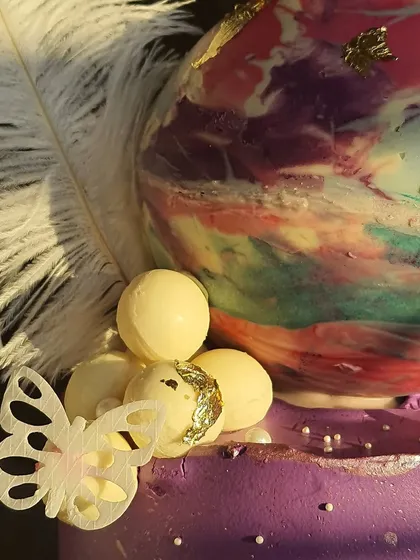 A close-up on the details of the galaxy-themed cake, showing the edible gold leaf on the chocolate sphere and the delicate wafer paper butterfly.