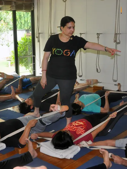 A class practices Supta Padangusthasana with belts. I am shown giving a correction, ensuring the students maintain proper alignment to get the maximum benefit from the stretch.