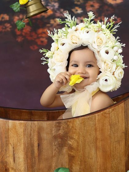 A close-up of the little girl in the floral bath theme, nibbling on a yellow petal with a sweet smile.