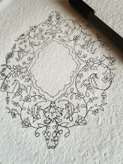 An intricate floral design being outlined with a fine-tipped pen, showing the detailed sketch work that goes into some pieces.