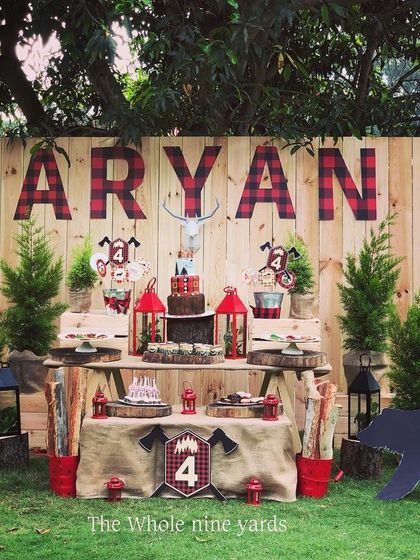 A rustic lumberjack-themed birthday party. The wooden backdrop with plaid lettering, mini pine trees, and a cutout bear created a fun outdoor adventure vibe.