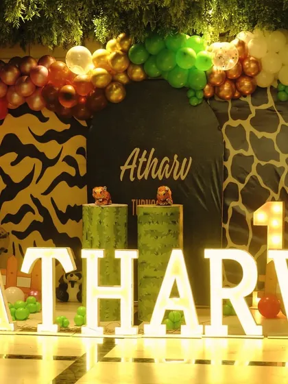 A vibrant jungle theme for Atharv's first birthday, featuring animal-print backdrops, marquee letters, and a colorful balloon arch.