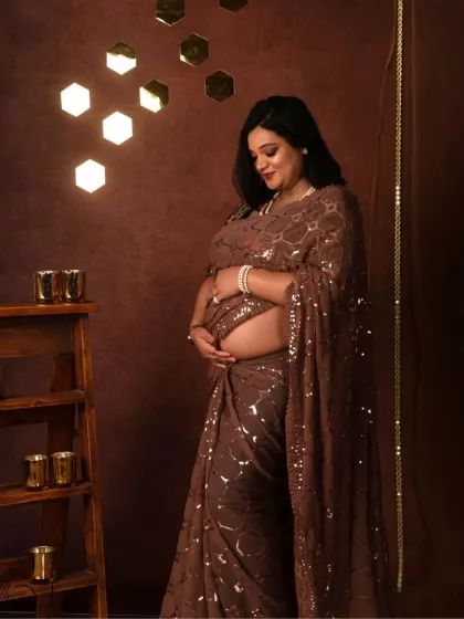 A quiet, intimate moment as she looks down at her bump. The warm lighting creates a beautiful, glowing effect on her skin and the saree.