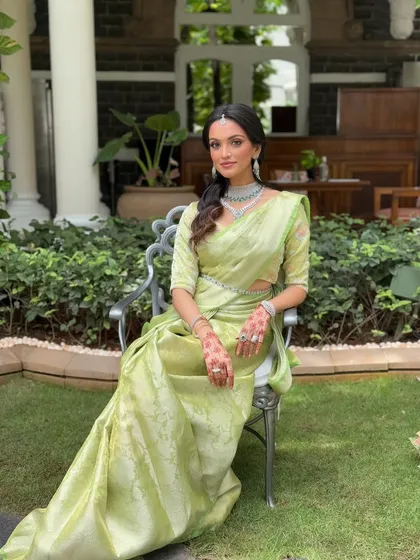A full-length seated portrait, showcasing the beautiful drape of the saree and the overall elegance of the look. The makeup is flawless from head to toe.