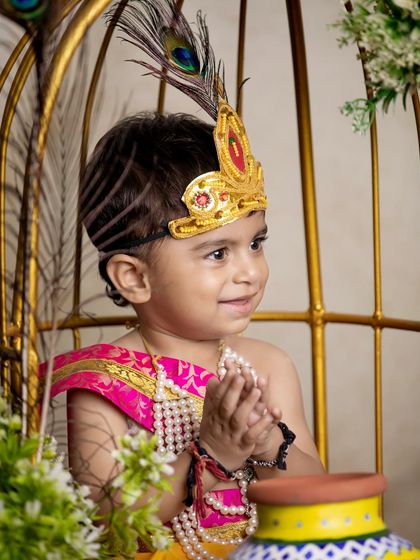 A smiling toddler dressed as Krishna, framed by a golden birdcage prop. This shot shows how I use larger props to create an interesting and playful composition.