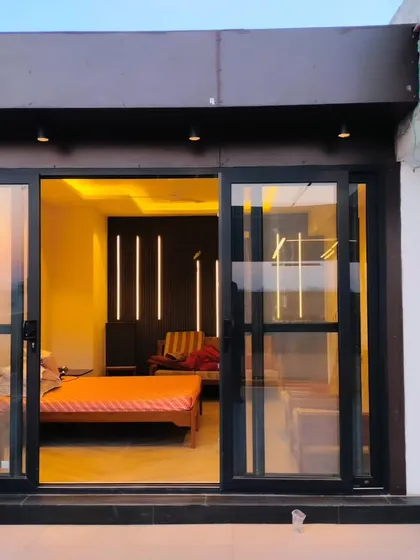 An exterior shot of the Palam Vihar terrace room at dusk, showing the warm interior lighting and its connection to the rooftop space.