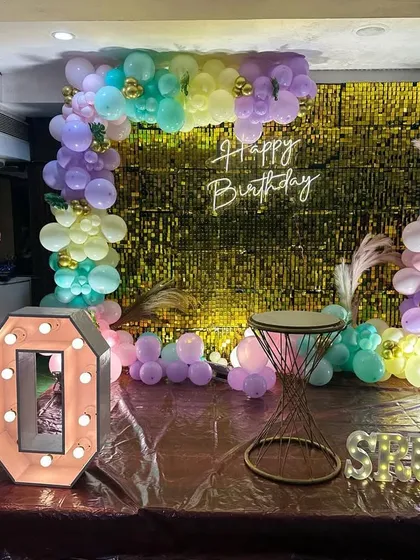 A fun and colorful 10th birthday decoration with a gold shimmer wall, pastel balloon arch, and large marquee numbers.